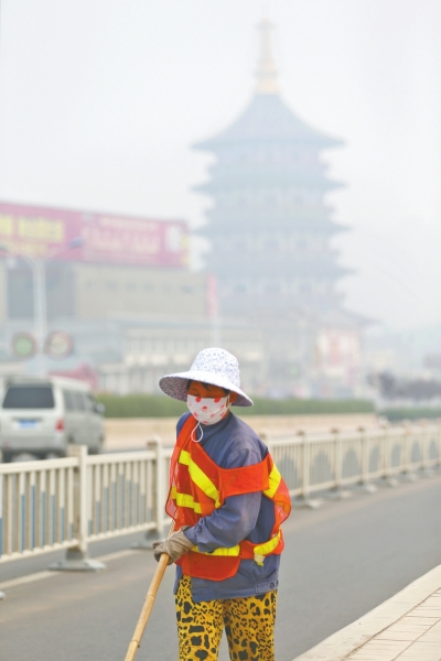 近日，在古都洛陽，環(huán)衛(wèi)工人身后的“天堂”被霧霾籠罩著。