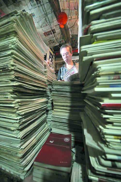 王曉民坐在寫字桌前，被報紙淹沒。