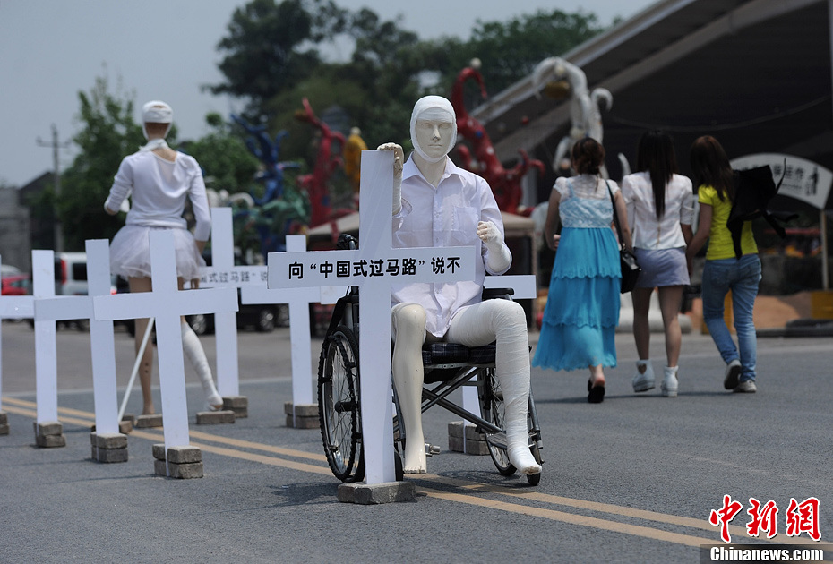 4月16日，重慶市洋人街上擺放著兩個(gè)受了傷的塑料人像“模特”，旁邊十字架上寫(xiě)著向“中國(guó)式過(guò)馬路”說(shuō)不