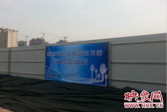 道路南側(cè)圍起了白色的圍擋，墻上標(biāo)示著“因地鐵施工帶來的不便敬請您諒解”的提示牌。