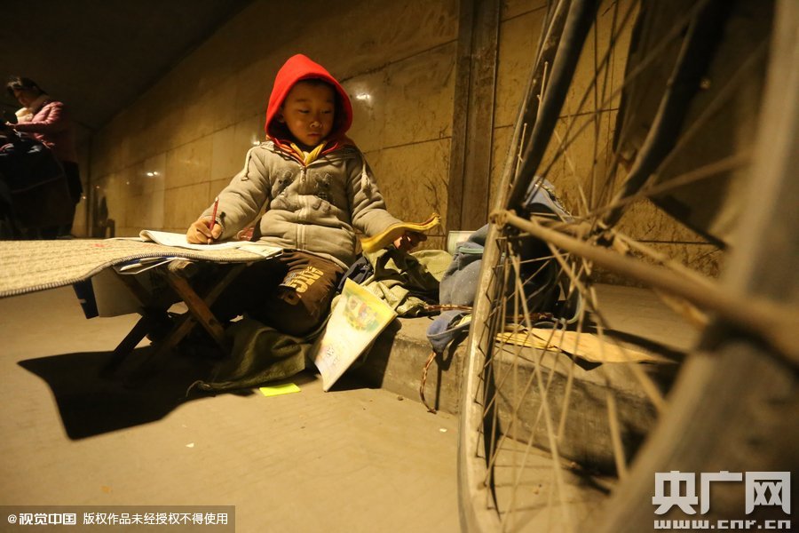 2015年11月8日晚，鄭州，7歲男孩涵洞橋下陪父母練攤，路邊燈下坐小馬扎上寫作業(yè)。