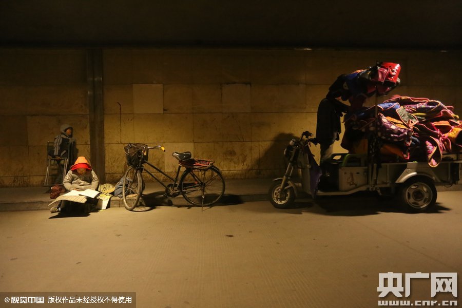 2015年11月8日晚，鄭州，7歲男孩涵洞橋下陪父母練攤，路邊燈下坐小馬扎上寫作業(yè)。